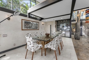 Elegant indoor dining area with table for eight with floor-to-ceiling glass walls, bringing in lush tropical views.