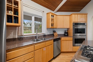 Your gourmet kitchen awaits with granite counters, stainless appliances, and warm wood cabinetry beneath exposed ceiling beams.