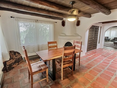 Dining area with kiva fireplace, dark viga ceilings, saltillo and white plaster for authentic New Mexican feel