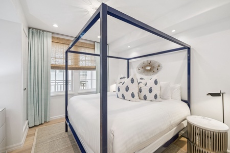 Drift off in this elegant four-poster bed with crisp white linens and charming patterned pillows in your serene coastal retreat.