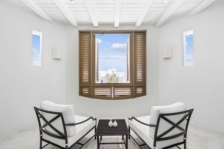 You'll find quiet moments here, where bright natural light meets clean white walls and comfortable seating—a serene retreat with glimpses of blue sky and soft coastal charm.