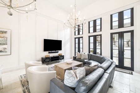 Relax in your bright, modern living room with soaring ceilings, elegant lighting, and floor-to-ceiling windows flooding the space with natural light.