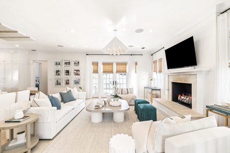 Unwind in this bright, sophisticated living room where plush white sofas surround a cozy fireplace and entertainment center for perfect evening relaxation.
