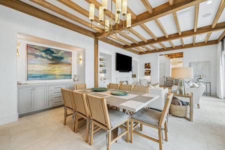 Gather around this spacious dining table under striking timber beams, where coastal artwork and elegant lighting set the stage for memorable meals together in your home away from home.