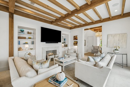 Picture yourself unwinding in this beautifully designed living space, where warm wood beams frame soaring ceilings and elegant built-ins surround the fireplace. Sink into plush seating as natural light fills your retreat.