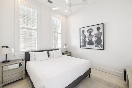 Sink into crisp white linens in your serene bedroom, where natural light streams through plantation shutters and modern art creates a sophisticated retreat.