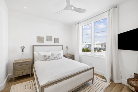 Relax in your serene bedroom, where soft linens, coastal artwork, and a ceiling fan create your perfect retreat. Natural light pours through the large windows.