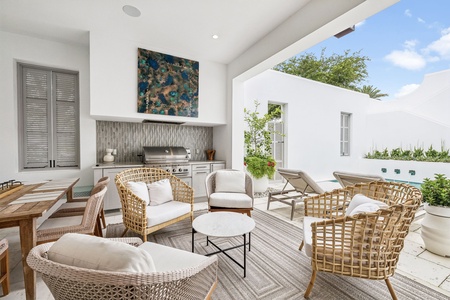 Relax in this elegant outdoor living space featuring woven lounge chairs with plush cushions, a built-in BBQ, and serene views of lush greenery—your perfect spot for entertaining or unwinding.
