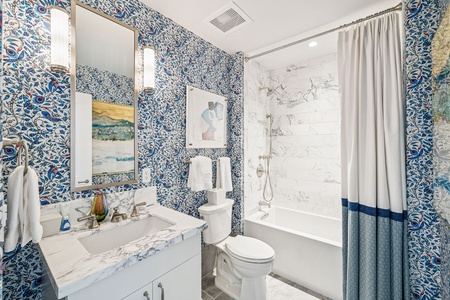 Immerse yourself in this stunning bathroom featuring vibrant blue botanical wallpaper, luxurious marble countertops, and a pristine shower-tub combo.