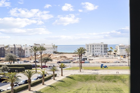 Ocean view from property window showcasing coastal buildings and palm-lined streets of the beachfront neighborhood.