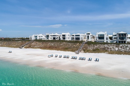 Pristine beachfront property set against turquoise waters and sugar-white sand, with rows of beach chairs awaiting guests beneath striped umbrellas.