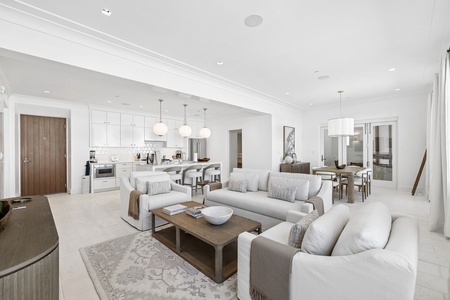 Bright, open living space where you can relax on plush sofas, gather around the dining table, or prepare meals in the modern, fully-equipped kitchen with sleek white cabinetry.