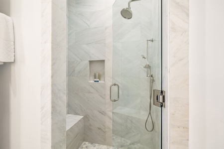 Rinse off beneath a rainfall showerhead in this bright marble-tiled walk-in shower. The built-in bench and niche add comfort and convenience.