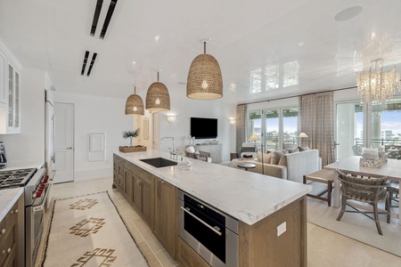 Your elegant kitchen island becomes the heart of this bright space, where natural woven pendant lights create warmth above marble countertops perfect for cooking.