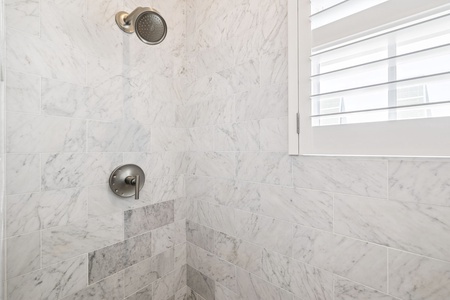 Step into your elegant marble shower featuring premium fixtures and natural light streaming through shuttered windows for a refreshing start.