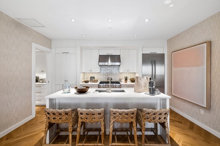 Your fully equipped kitchen features sleek white cabinetry, stainless steel appliances, and a spacious island with seating for four—perfect for preparing meals together or enjoying morning coffee.