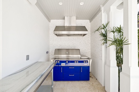 Your outdoor culinary dreams come alive in this stunning covered kitchen featuring a brilliant blue commercial-grade range and professional ventilation system.