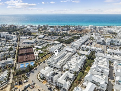 Aerial view of the coastal resort community featuring modern white buildings, tennis courts, and pristine beachfront just minutes away.