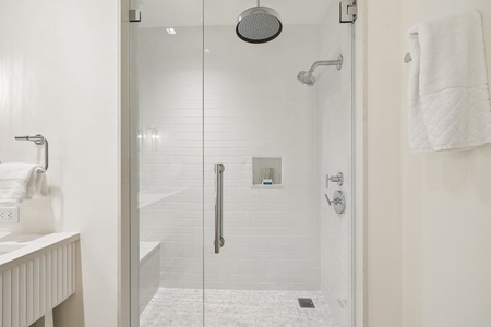 Step into your serene spa-like shower with dual rainfall and handheld heads, white subway tile, and gleaming glass doors waiting to refresh you.