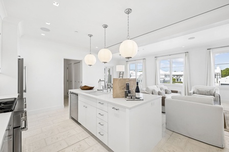 Sunshine streams into your open-plan living space, where the sleek kitchen island invites meal prep and conversation, while the plush living area beckons you to unwind in coastal serenity.