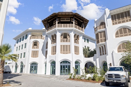 A striking white Mediterranean-style building features ornate architectural details, including decorative trim and elegant arched windows, set against a bright blue sky.