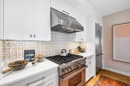 Prepare your favorite meals in this beautifully appointed kitchen featuring modern stainless steel appliances, elegant white cabinetry, and eye-catching geometric tile backsplash that adds character to your cooking space.