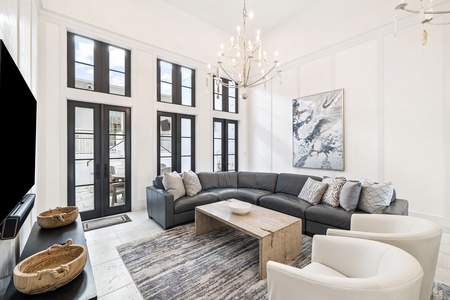 Sink into your spacious sectional beneath soaring ceilings and elegant chandeliers, where floor-to-ceiling windows flood this sophisticated living space with natural light.