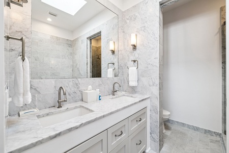 Indulge in this spa-like marble bathroom with dual sinks, modern fixtures, and natural light through the skylight above.