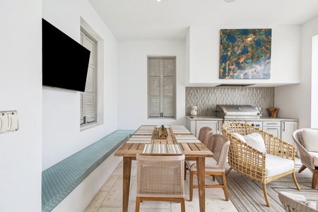 Gather around this inviting coastal dining space where woven chairs and a custom bench with turquoise cushions surround a beautifully crafted wood table beneath vibrant abstract art.