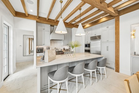 Picture yourself preparing meals in this bright, sophisticated kitchen with gleaming marble countertops, designer lighting, and beautiful exposed wood beams overhead. The spacious island invites gathering and conversation.
