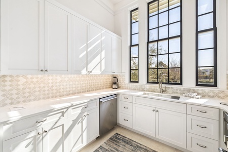 Sunlight streams through tall windows into your bright, modern kitchen with marble counters and premium appliances.