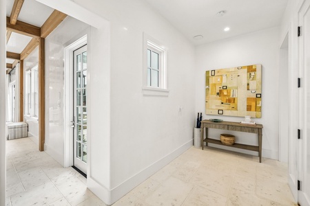 Step into your bright, airy entrance where natural wood beams and coastal charm blend beautifully. Your peaceful retreat begins here, with sunlight streaming through glass doors.