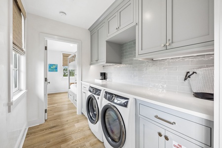 Your dedicated laundry room features modern front-loading machines, ample countertop space for folding, and soft gray cabinetry with elegant subway tile backsplash—making wash day feel effortless and organized.