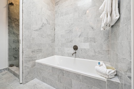 Unwind in your elegant marble bathroom featuring a luxurious soaking tub and spacious walk-in shower with plush towels.