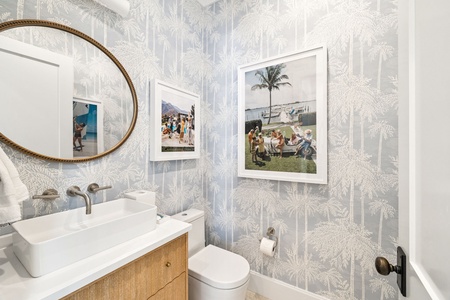 Your powder room features tropical palm wallpaper, modern fixtures, and charming vintage coastal artwork that sets a relaxed vacation mood.