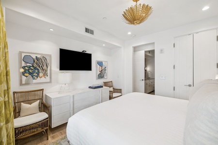 Relax in your serene bedroom featuring crisp white linens, elegant artwork, and a mounted TV for cozy evenings in.