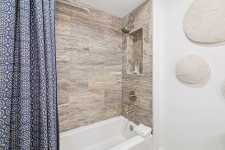 Unwind in your spa-like bathroom featuring elegant stone tiling, a deep soaking tub, and rainfall shower.