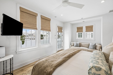 Sink into crisp white linens in your sun-drenched bedroom, where natural light floods through elegant windows and a ceiling fan keeps you perfectly comfortable year-round.