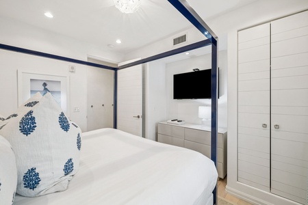 Drift into dreams in your elegant bedroom with its stylish navy canopy bed, crisp white linens, and modern TV for cozy nights in.