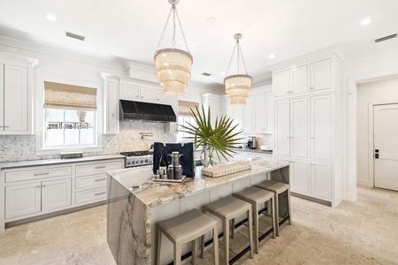 Cook with luxury in this pristine white kitchen featuring elegant chandeliers and premium appliances perfect for your culinary adventures.