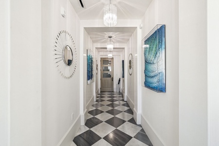 Step into your grand hallway with stunning checkerboard floors, crystal chandeliers, and elegant coastal artwork guiding you home.