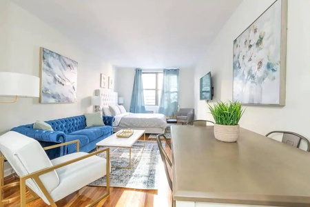 Unwind in your stylish studio with plush blue velvet sofa, modern artwork, and abundant natural light streaming through oversized windows.