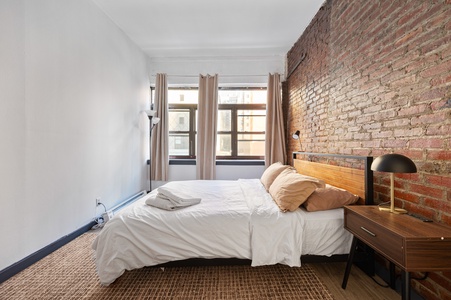 Relax in your stylish bedroom featuring exposed brick walls, crisp linens, and warm wood accents that create the perfect urban retreat.