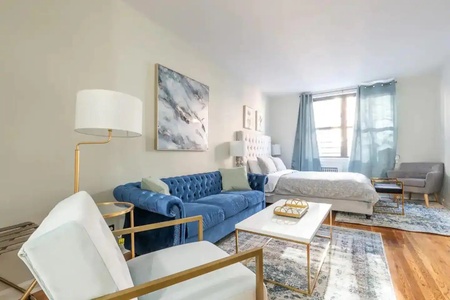 Sink into the plush blue sofa in your bright, airy studio where golden accents and natural light create the perfect retreat.