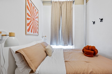 Sink into crisp linens and soft pillows in your peaceful retreat, where warm orange accents and natural light create the perfect atmosphere for rest.