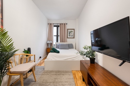 Unwind in your bright, plant-filled bedroom featuring a comfy white bed, modern TV, and stylish wooden accents that create a peaceful urban retreat.