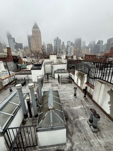 Urban rooftop terrace offers dramatic Manhattan skyline views, including the iconic Empire State Building piercing through misty clouds.