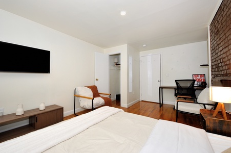 Your stylish bedroom features crisp white bedding, exposed brick walls, and a dedicated workspace with modern amenities.