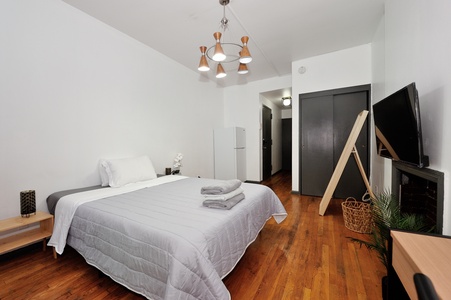 Unwind in your modern bedroom featuring warm hardwood floors, stylish lighting, and thoughtful touches like fresh towels and greenery.