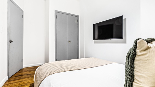 Unwind in your cozy bedroom with plush bedding, modern amenities, and a wall-mounted TV for your relaxation.